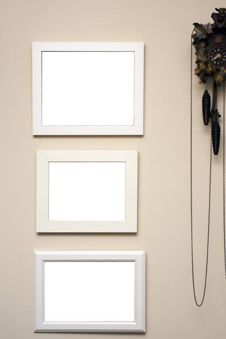 Free Stock Photo: Three empty frames hanging on a beige colored wall alongside a wooden carved cuckoo clock with pendulums