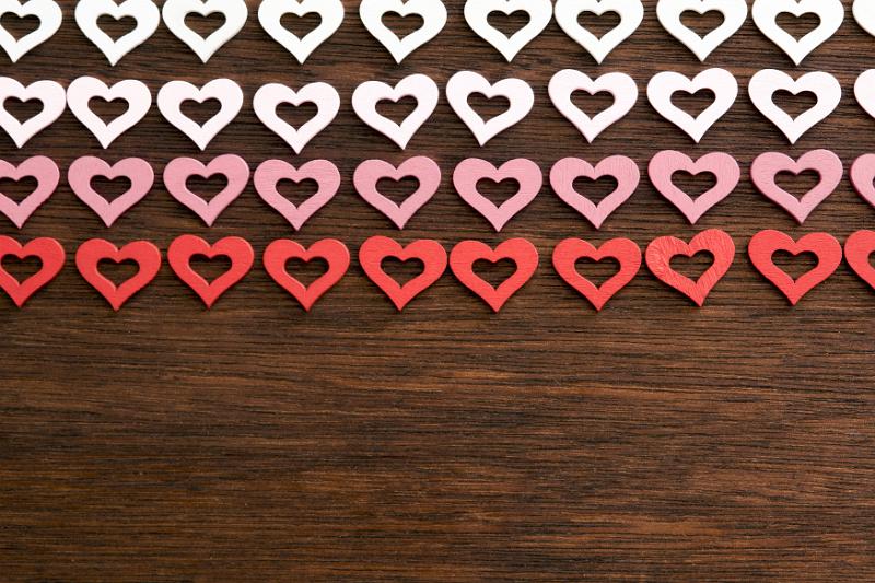 Free Stock Photo: Romantic border of colored hearts in white pink and red arranged in rows on a textured wooden background with copy space