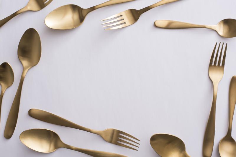 Free Stock Photo: Border of elegant gold cutlery with spoons and forks arranged randomly around central white copy space for food or catering themes