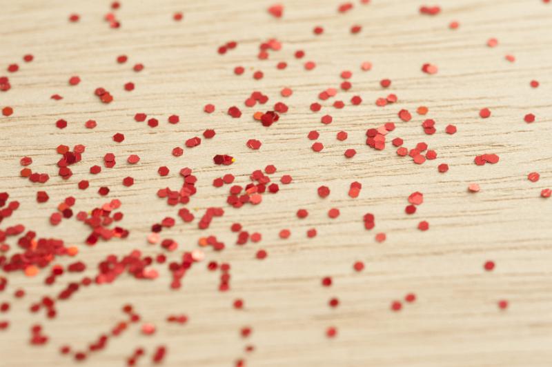 Free Stock Photo: Scattered glittering red sequins on a wooden background for a festive or party concept with shallow DOF
