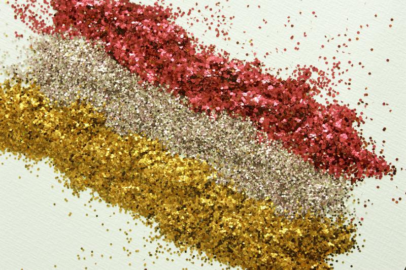 Free Stock Photo: Gold and red glitter pattern with three lines of yellow and rose gold and red at a diagonal angle on a white background, high angle view for Christmas or festive occasions