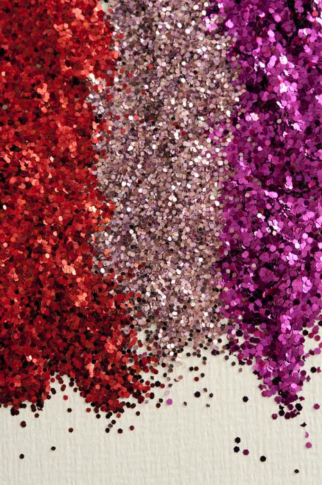 Free Stock Photo: Colorful festive piles of red, pink and purple glitter for craft work arranged in three vertical lines over a textured white background with copy space