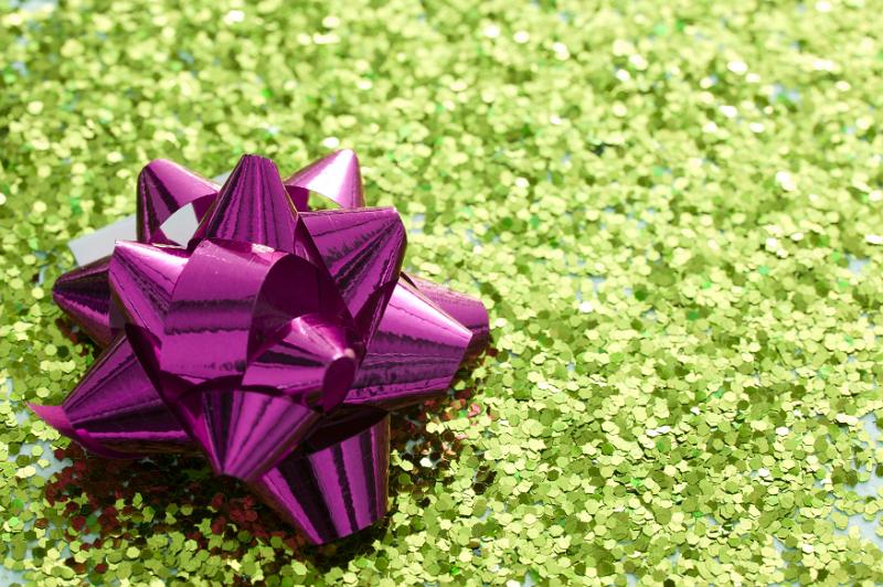 Free Stock Photo: Holiday or gift concept of shiny purple bow in corner of green sparkling glitter background with copy space