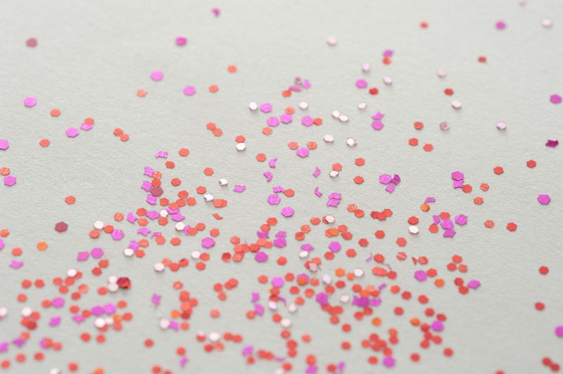 Free Stock Photo: Scattered pieces of red and pink glitter sprinkled on gray paper as background