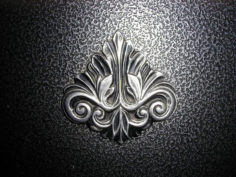 Free Stock Photo: Acanthus leaf decoration on a fireplace in raised relief against a textured pitted background, central highlight on the decoration
