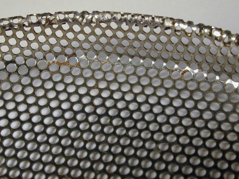 Free Stock Photo: Close up view of shiny metal sheet perforated with many small holes against a gray background