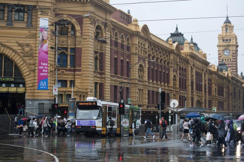 Free Stock Photo: Busy street scene in Melbourne, Australia on a rainy day with passengers and a tram in front of the entrance to the Flinders Street station