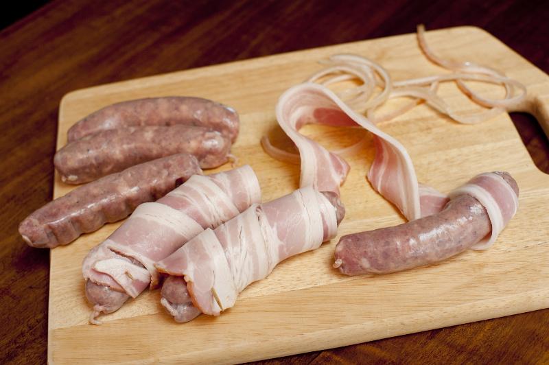 Free Stock Photo: It wouldn't be Christmas: Preparing bacon rolls on a wooden board in the kitchen with spicy sausages and rashers of smoked bacon for the wrapper