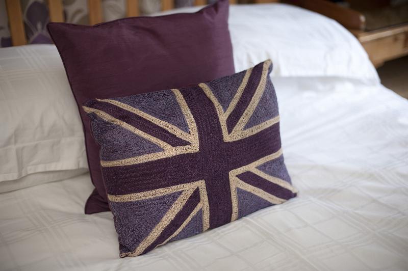 Free Stock Photo: Patriotic British themed bedroom with cushions bearing the Union Jack flag on the bed on white linen, close up view