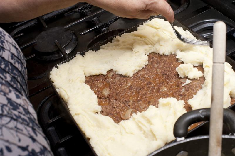 Free Stock Photo: Cooking cottage pie adding the mashed potato topping or crust to the savory mince meat