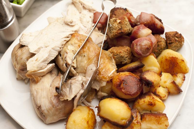 Free Stock Photo: Carved roast chicken, roast potato and vegetables on a plate with metal thongs ready to be served for dinner