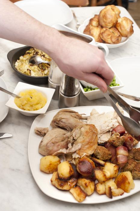 Free Stock Photo: Man serving a family roast dinner using a pair of tongs to dish up carved chicken or turkey from a table laid with vegetables and sauces