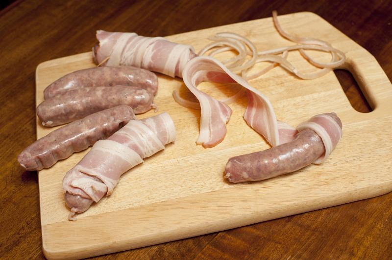 Free Stock Photo: Making bacon rolls with spicy sausages wrapped in rashers of cured bacon laid out on a wooden board in the kitchen