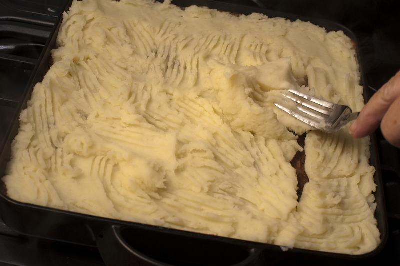 Free Stock Photo: Preparing Shepherds pie in the kitchen smoothing the mashed potato topping or crust over the minced meat with a fork, close up view of the oven dish