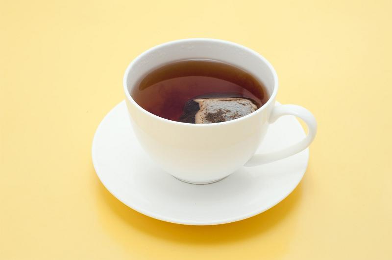 Free Stock Photo: Teabag steeping in a cup of fresh hot tea to obtain the desired strength of the brew in a plain white cup and saucer on a yellow background