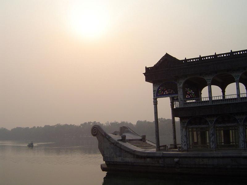 Free Stock Photo: Detail of House Boat with Ornate Carvings Floating on Calm River with Small Boat and Shoreline in Background Under Hazy Sky with Obscured Sun
