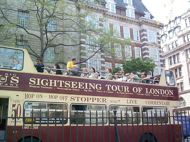 Free Stock Photo: London double decker sightseeing bus with its open upper deck filled with tourists view side angle in a city street with the signage visible on the side,