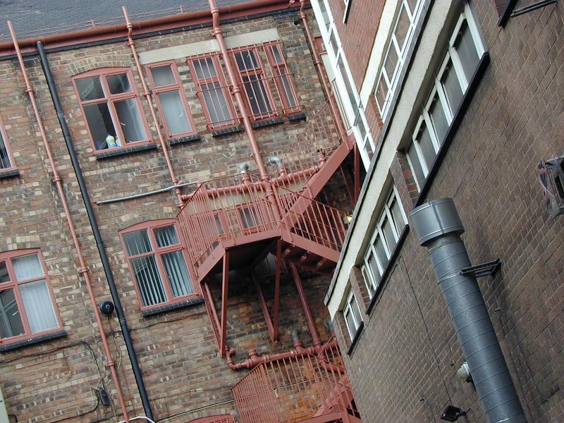 Free Stock Photo: Red metal fire escape on the exterior of a an old face brick building viewed at a tilted angle from below