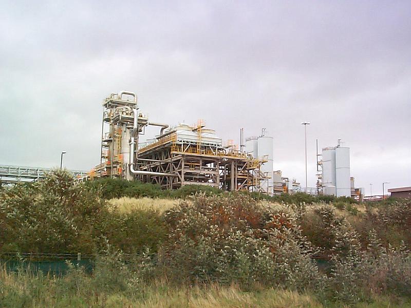 Free Stock Photo: Skyline view of an industrial production plant against a cloudy sky viewed over bushes and scrub