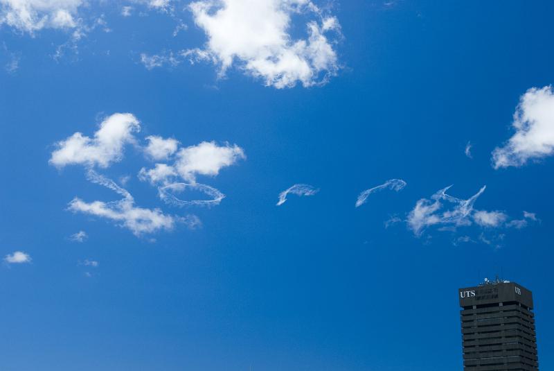 Free Stock Photo: Word Sorry written across a sunny blue sky in smoke emissions with a lone high-rise building below