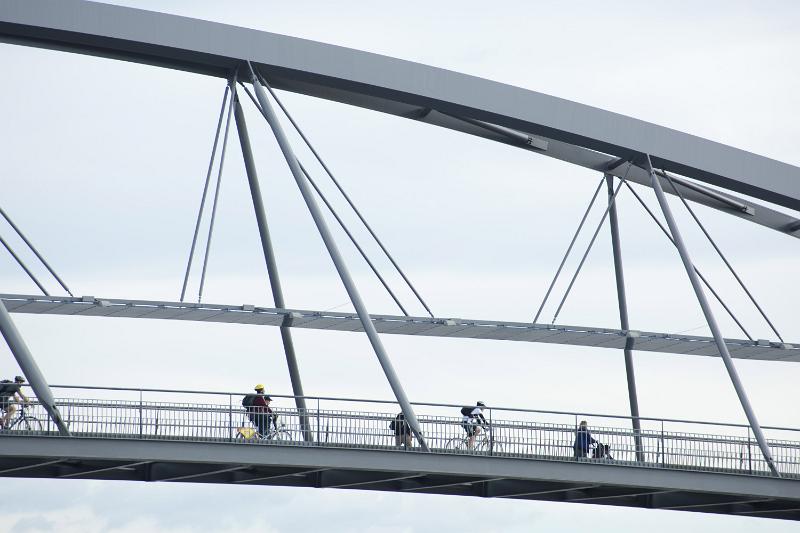 Free Stock Photo: People walking and cycling across a pedestrian bridge silhouetted against a high key sky in a structural engineering and architecture concept