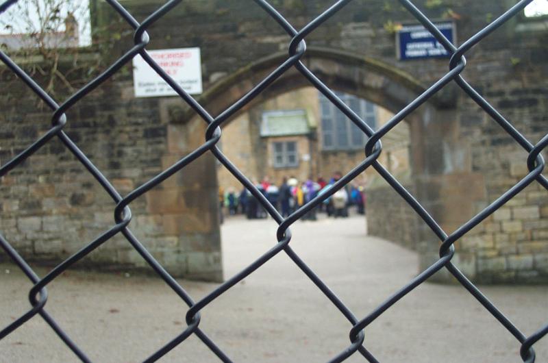 Free Stock Photo: Looking through a school fence at a distant group of students gathered in a courtyard
