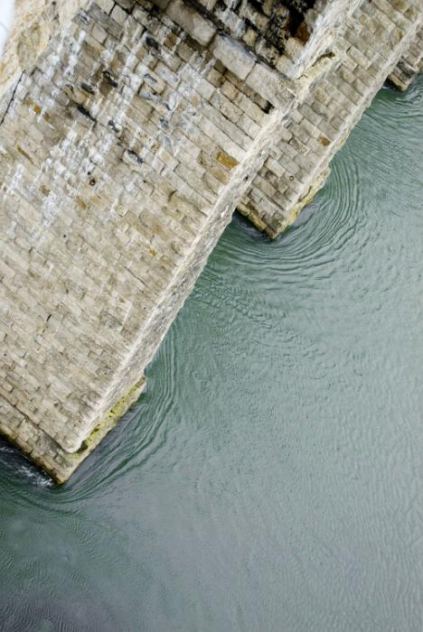 Free Stock Photo: View over the side of an old stone bridge at the water below eddying around the supports as the river flows under the span