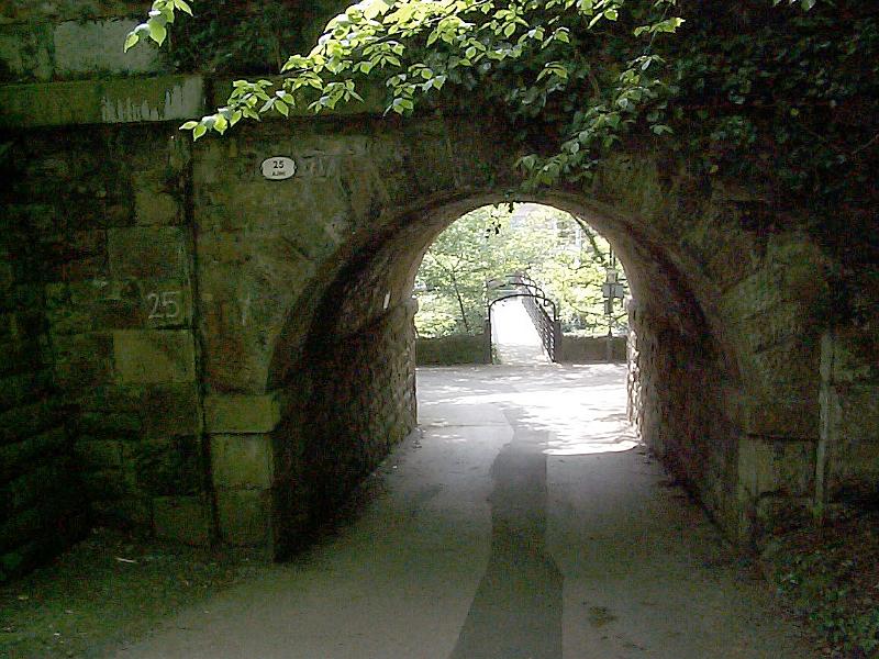 Free Stock Photo: Pass under the arch through an old thick stone wall with green foliage