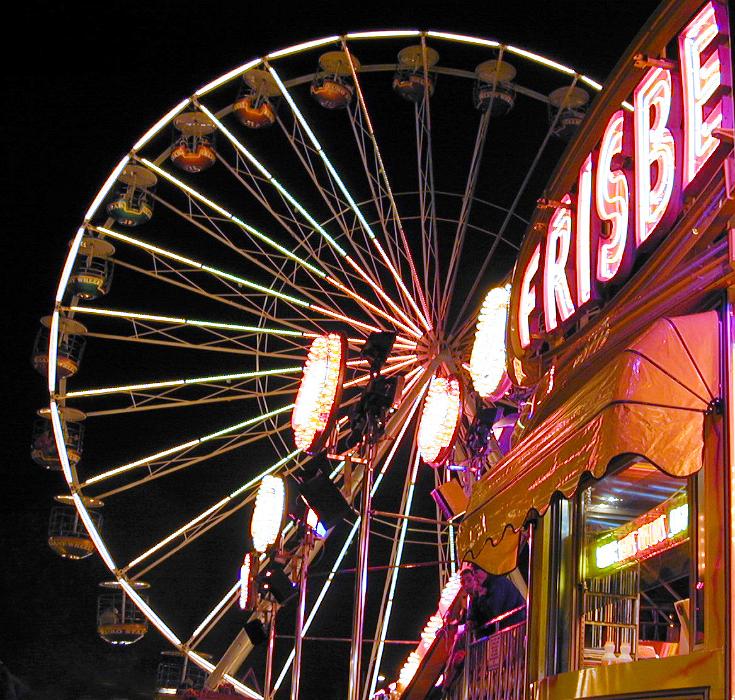 Free Stock Photo: Brightly lit stalls and illuminated ferris wheel at a fairground or amusement park at night in a close up view