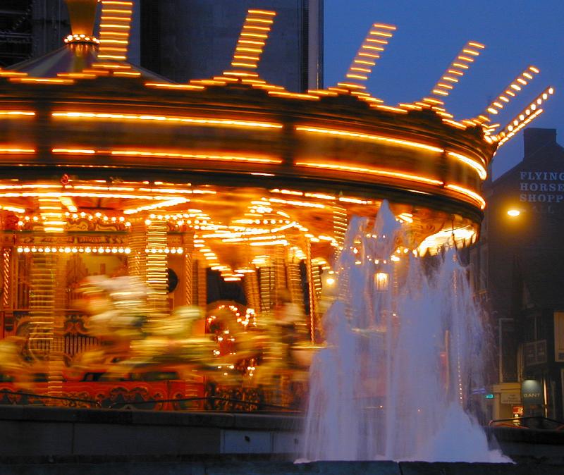 Free Stock Photo: Motion blur on a brightly lit festive spinning merry-go-round at night with foreground fountain