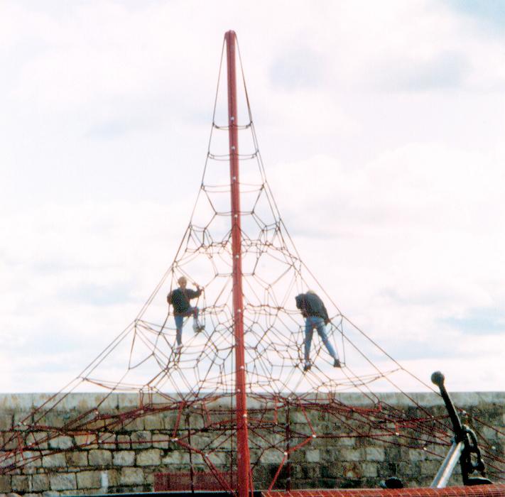 Free Stock Photo: Two young men climbing on a exterior tall play frame in front of an old stone wall an overcast sky