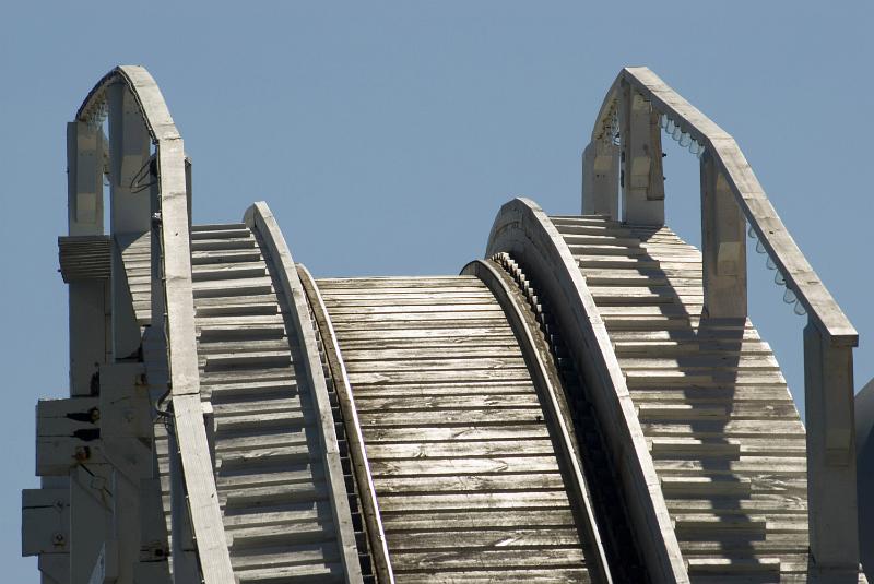 Free Stock Photo: Empty rollercoaster track and safety rails cresting a steep hill against a sunny blue sky at an amusement park