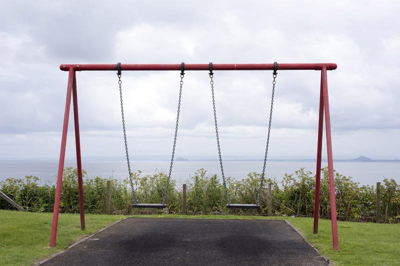 Free Stock Photo: An empty swing set in a park with a view of the ocean on a cloudy day.