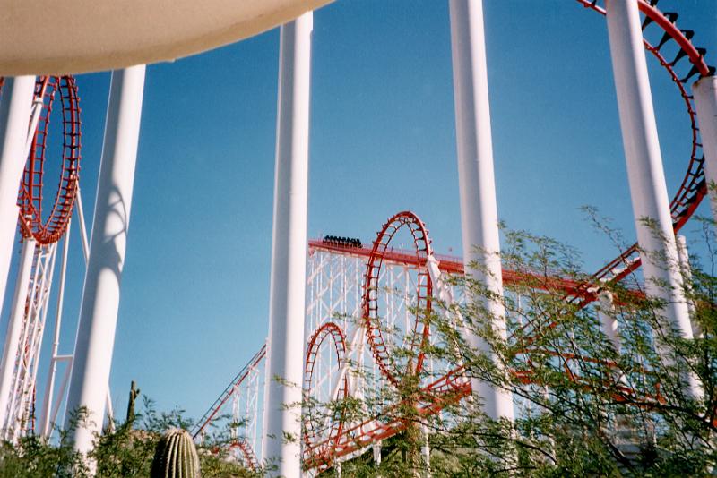 Free Stock Photo: Looking up between the support columns at the looping track of a colorful red rollercoaster ride at an amusement park against a blue sky