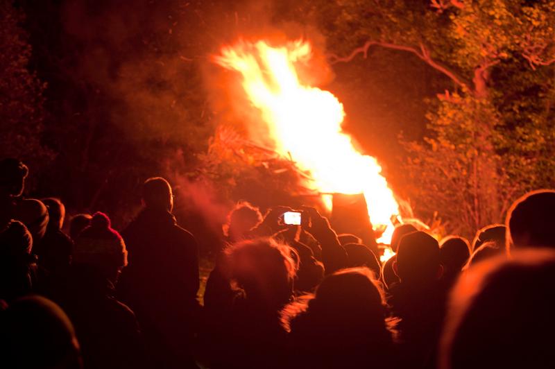 Free Stock Photo: Crowd of people gathered around a bonfire with a large column of bright orange flames shooting into the air at night