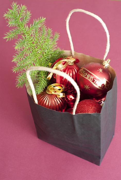 Download image of Paper bag full of colourful Christmas decorations Free Stock Photo: Paper bag filled with colourful Christmas decorations with red baubles and a small pine Xmas tree over a red background
