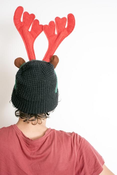 Free Stock Photo: Rear view of a person wearing a colorful red reindeer Christmas hat with antlers facing a white wall with copy space