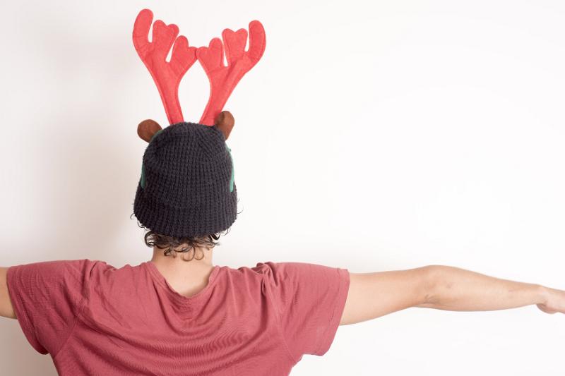 Free Stock Photo: Young person wearing a Christmas hat with festive red reindeer antlers standing with back to the camera over a white wall and copy space