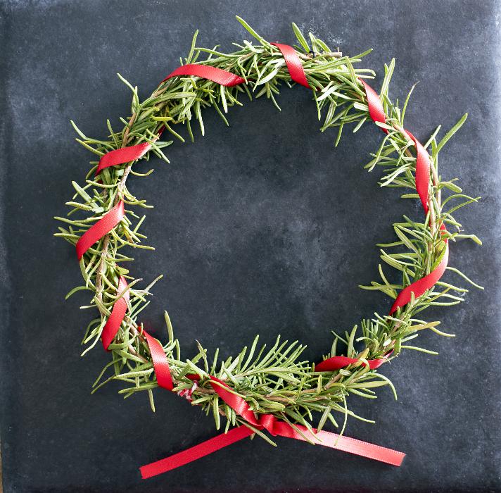 Free Stock Photo: Homemade Christmas wreath with rosemary foliage and a twisted red ribbon over a textured dark background with copy space