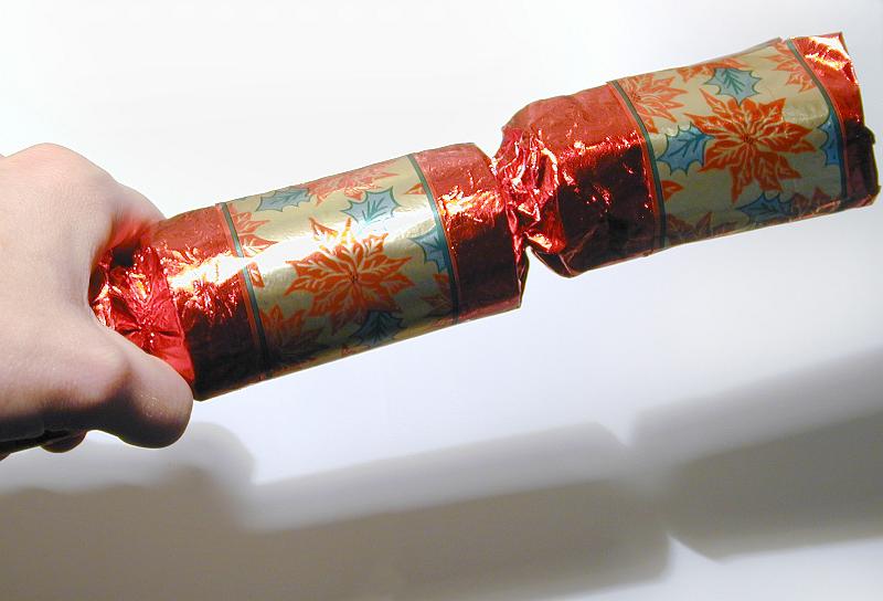 Free Stock Photo: Male hand holding a colorful red Christmas cracker table decoration ready to pull it with a friend over a white background