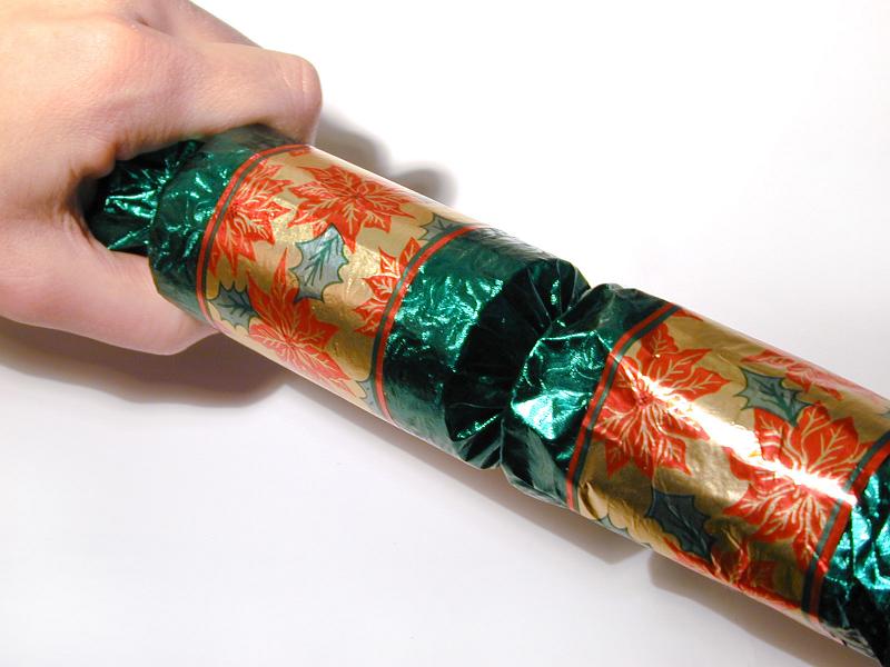 Free Stock Photo: Man ready to pull a colorful green Christmas cracker decorated with poinsettia flowers, holding the one end in his hand over a white background