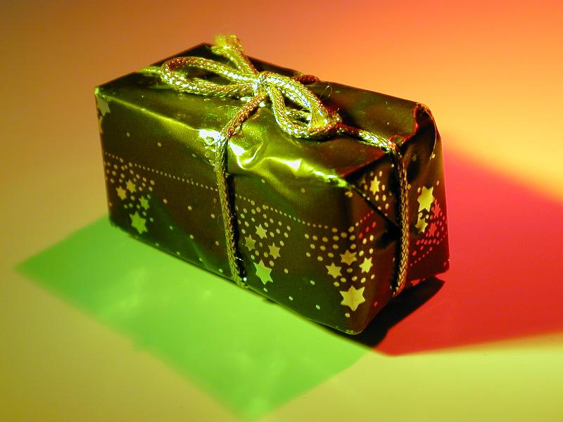 Free Stock Photo: Small Christmas present in colorful lighting wrapped in star decorated paper and tied with gold string