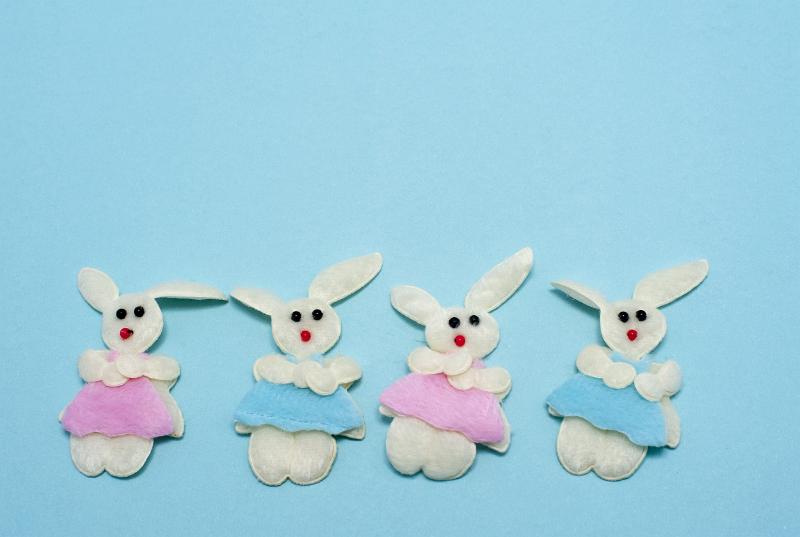 Free Stock Photo: Four needle work fluffy white Easter bunnies in pink and blue clothes on blue background with copyspace.