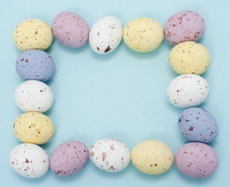 Free Stock Photo: Frame with blank copyspace bordered by speckled candy Easter eggs in pastel shades of pink, yellow, white and blue, blue background.