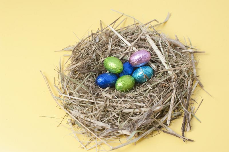 Free Stock Photo: Colourful foil wrapped chocolate Easter Eggs in a straw nest on yellow background.
