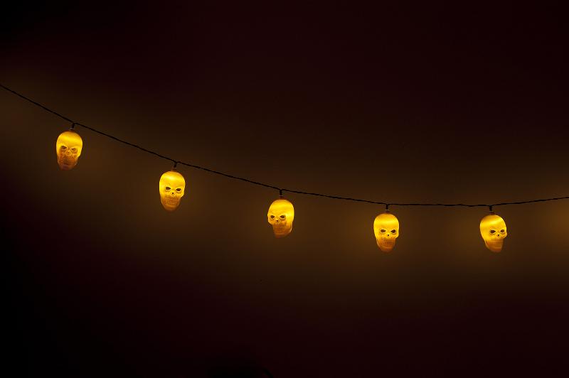 Free Stock Photo: Still Life of String of Illuminated Halloween Skull Lights Suspended in Eerie Dark Room Against Plain Wall with Copy Space