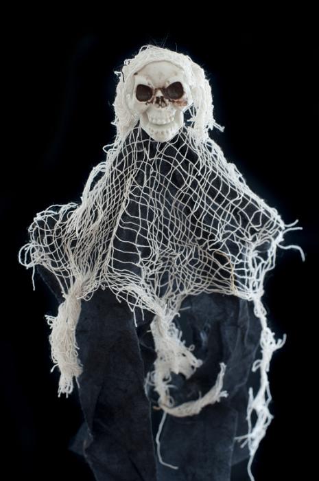 Free Stock Photo: Spooky Halloween witch doll with frayed rustic hessian fabric around a skull with spooky dark eye sockets isolated on a black background
