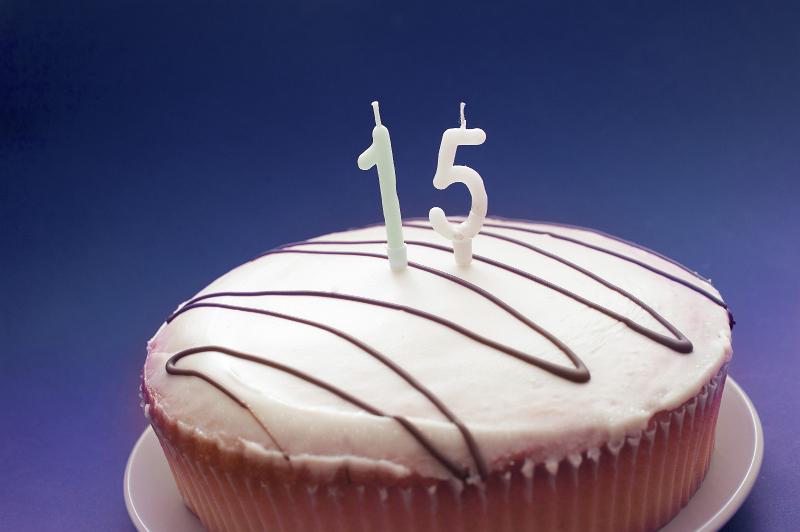 Free Stock Photo: Close Up of Birthday Cake in Paper Wrapper with Candles for 15th Birthday, Vanilla Icing Drizzled with Chocolate on Blue Background