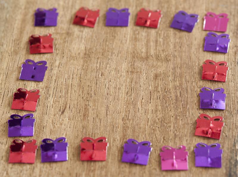 Free Stock Photo: Purple, Pink and Red Foil Confetti Shaped Like Gifts Arranged into Square Border on Wooden Background
