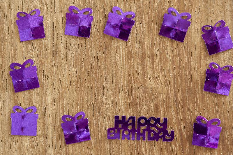 Free Stock Photo: Purple Metallic Birthday Confetti Arranged in Square Border on Wooden Background, Shaped like Wrapped Presents with Birthday Message in Middle
